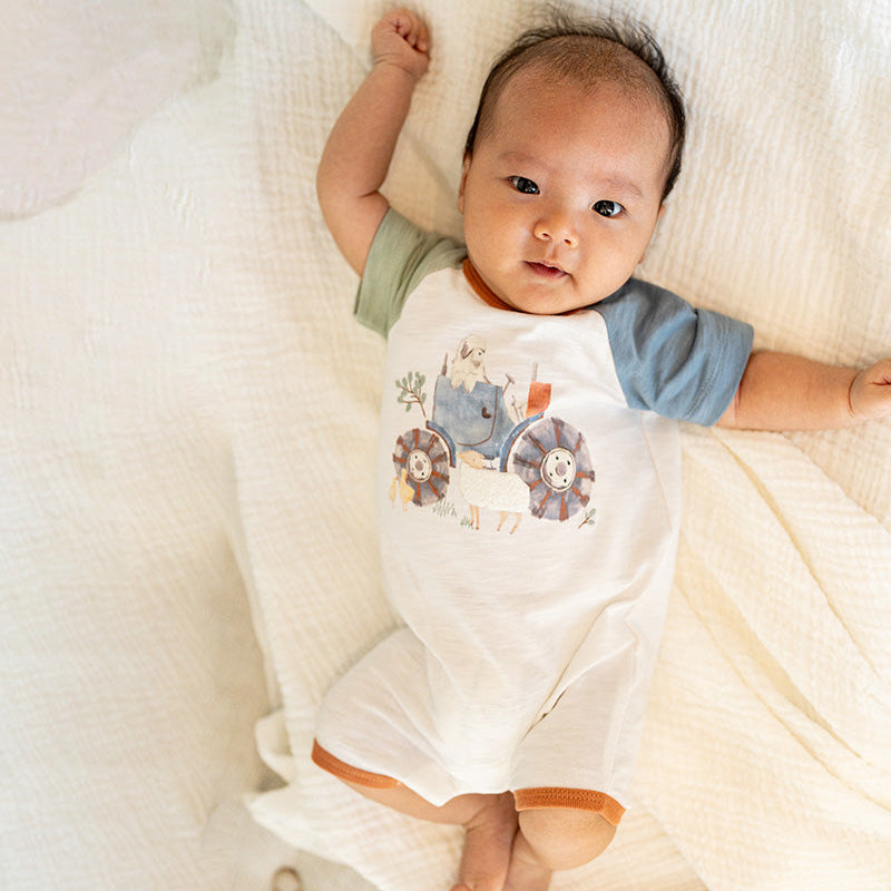 Baby romper in white with green and white sleevews and a tractor print on the front.