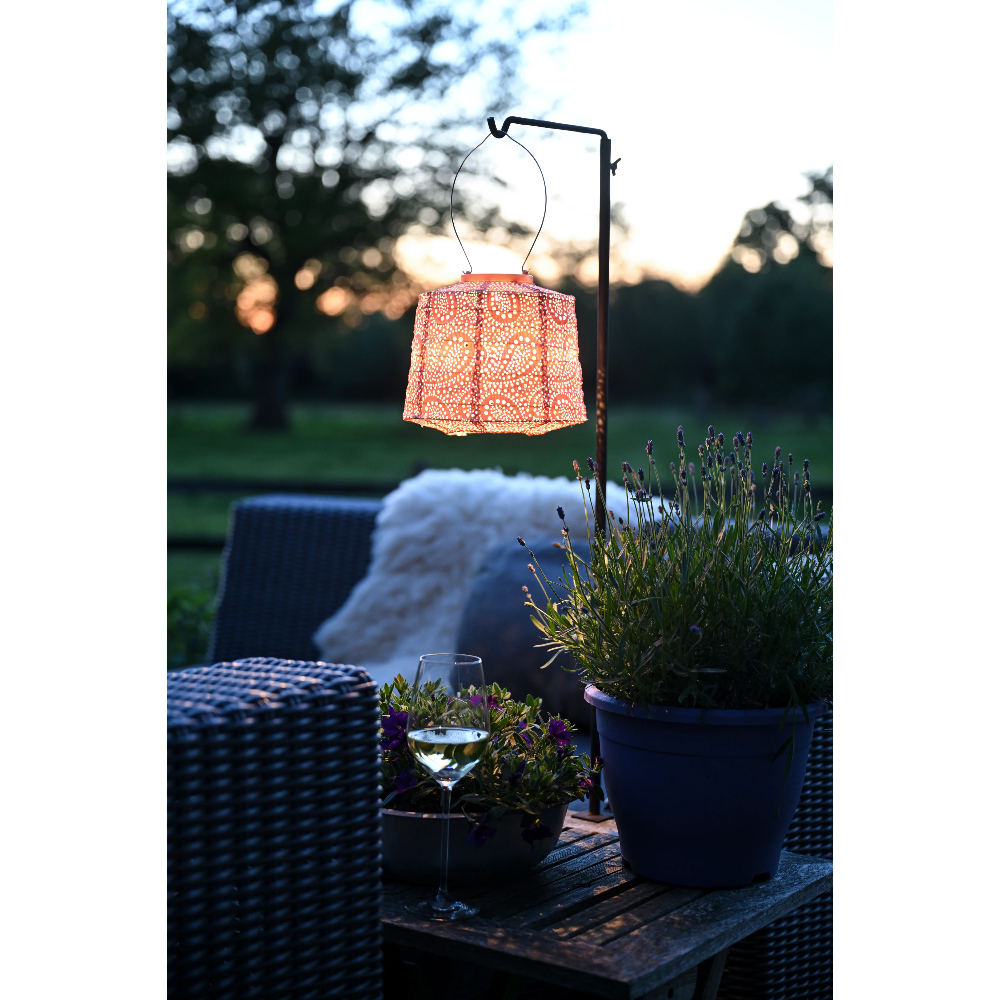 Outdoor setting with a solar lantern on a stand, surrounded by plants and furniture.