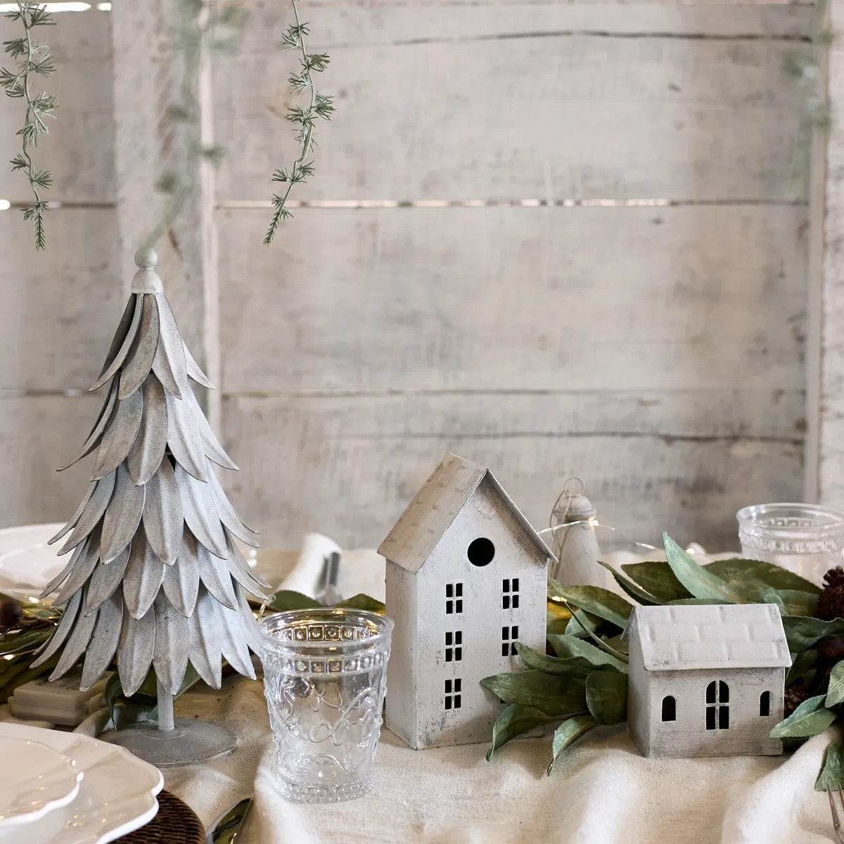 Decorative table setting with small houses, a tree, and greenery on a neutral background
