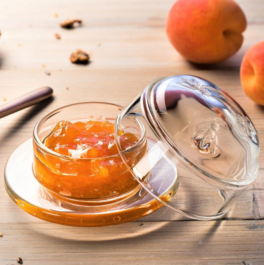 Glass container with peach compote on a wooden surface with peaches and cinnamon sticks.