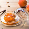 Glass container with peach compote on a wooden surface with peaches and cinnamon sticks.