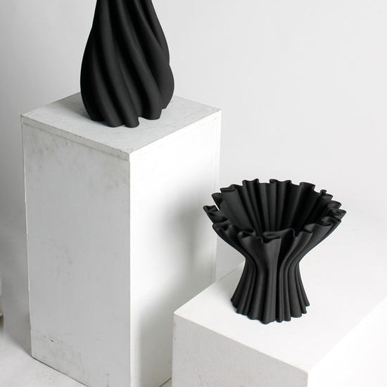 Two black vases on white pedestals against a light gray background
