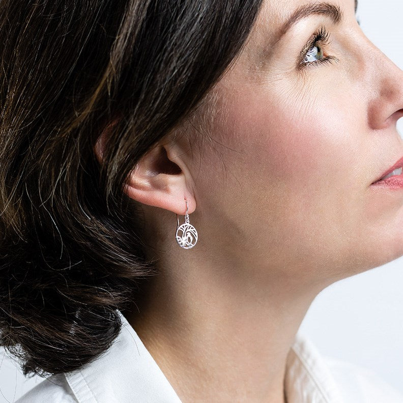 Model wearing silver drop earrings in a circular shape featuring the New Zealand Kereru Bird