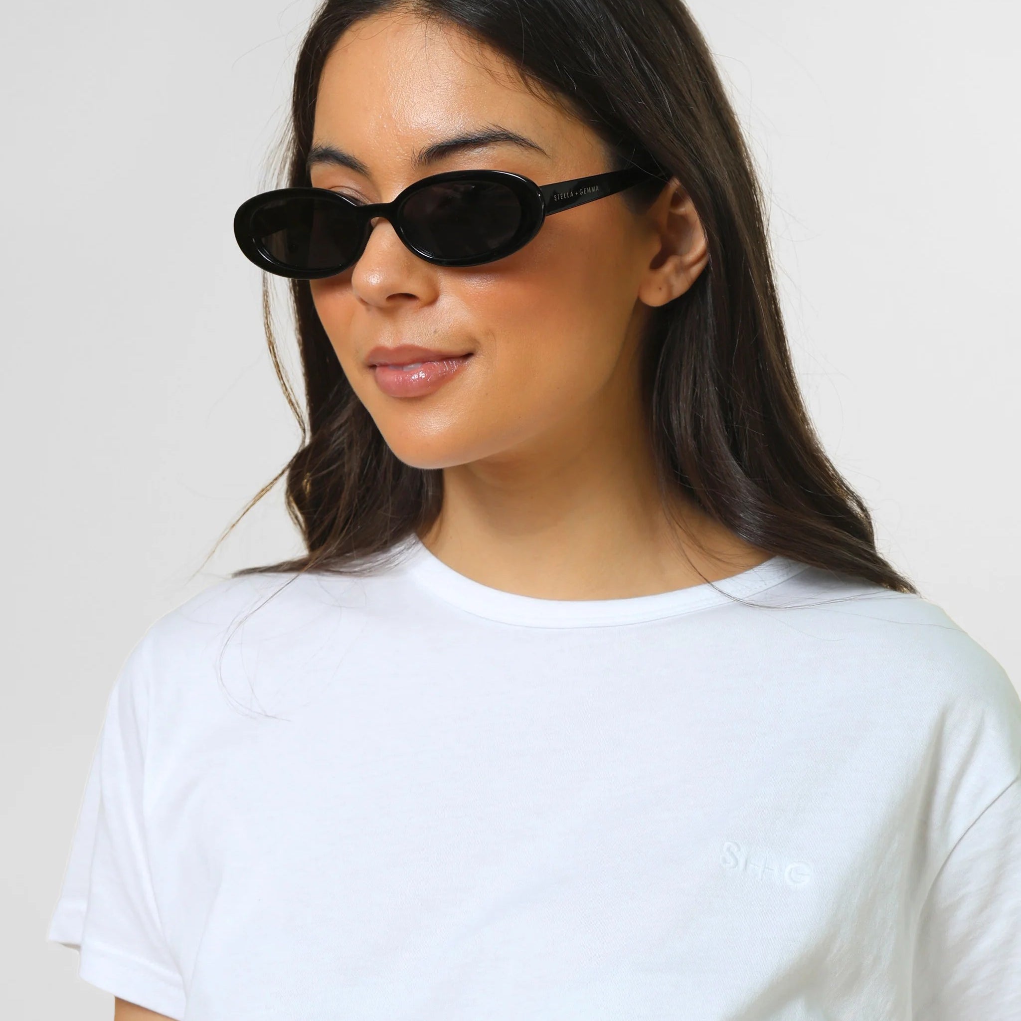 Woman wearing black cat-eye sunglasses and a white t-shirt against a plain background