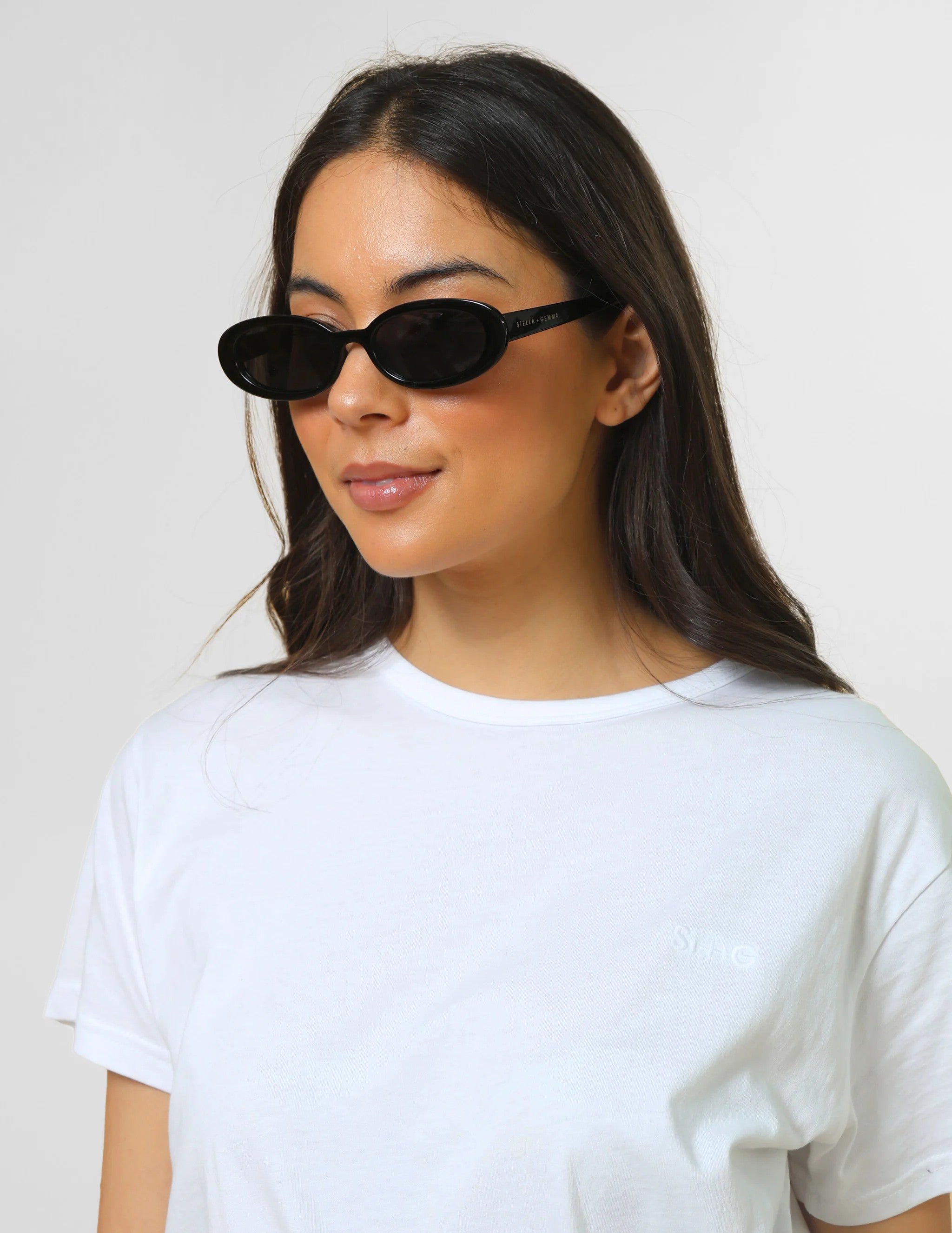 Woman wearing black cat-eye sunglasses and a white t-shirt against a plain background
