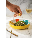 Person squeezing lemon over a salad in a colorful yeallow, orange and green bowl