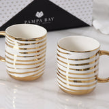 Two white mugs with gold stripes on a light surface, with 'Pampa Bay' branding in the background.