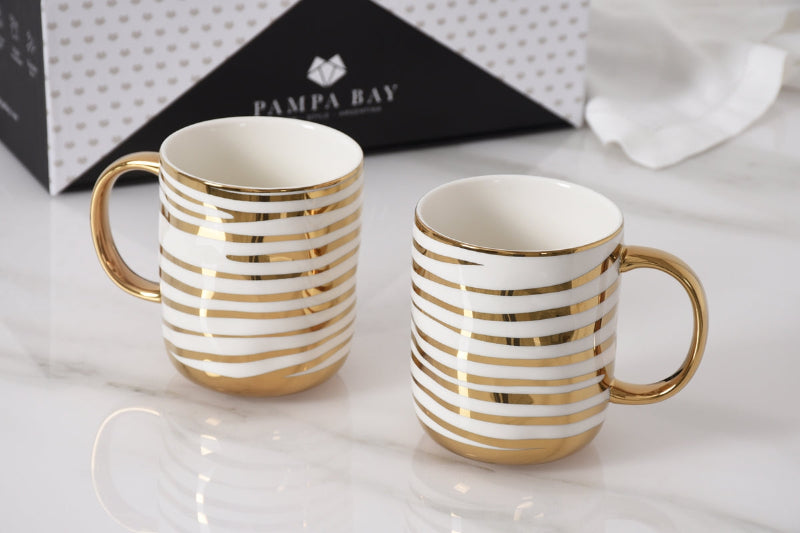 Two white mugs with gold stripes on a light surface, with 'Pampa Bay' branding in the background.