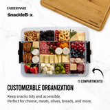 Farberware SnackleBox with various snacks and a wooden cutting board on a white background