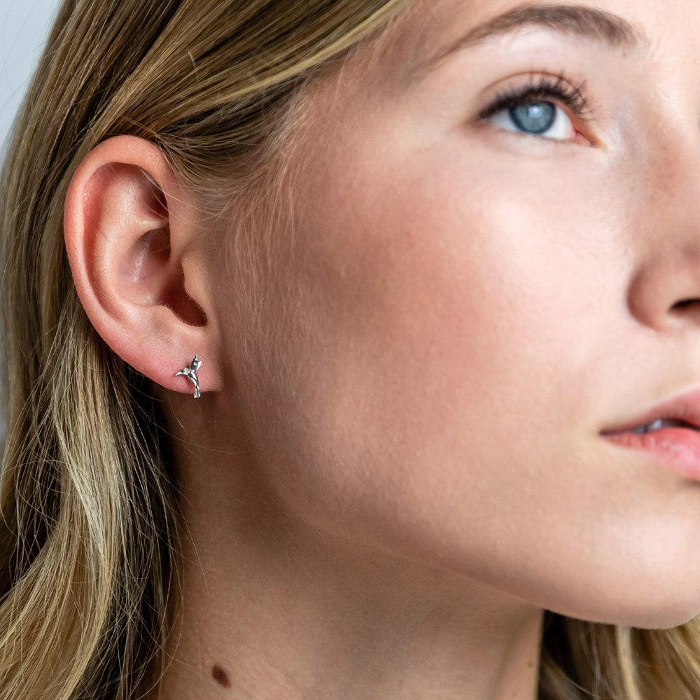 A woman wearing silver studs featuring a hummingbird