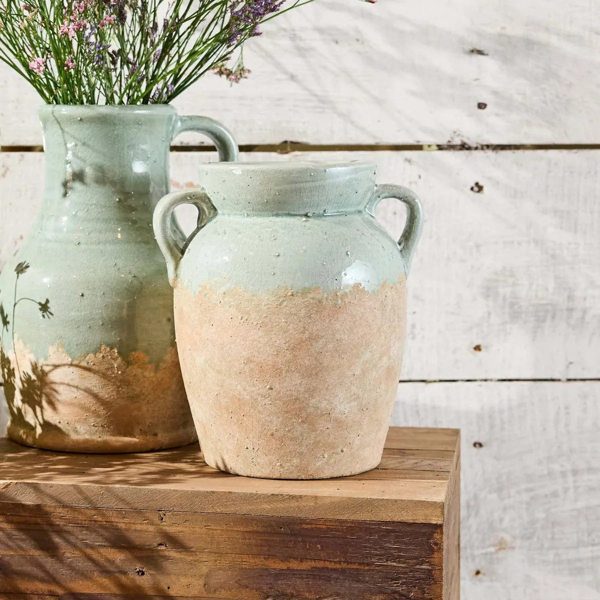 Two ceramic vases on a wooden surface with a rustic background