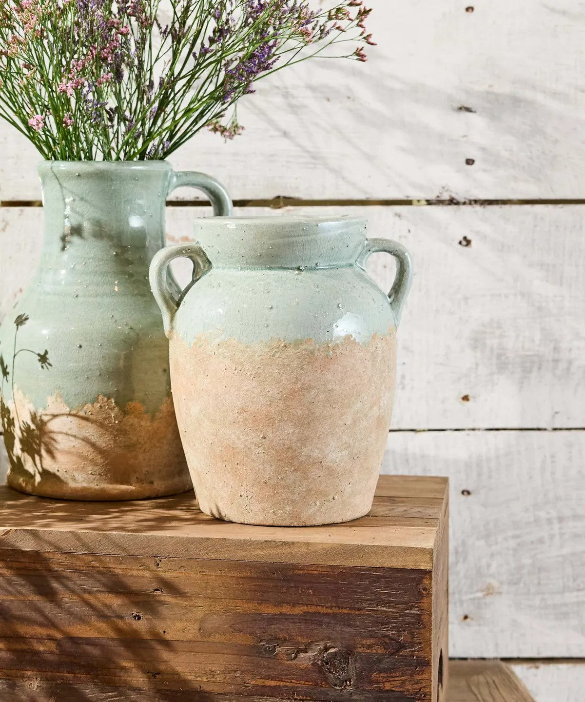 Two ceramic vases on a wooden surface with a rustic background