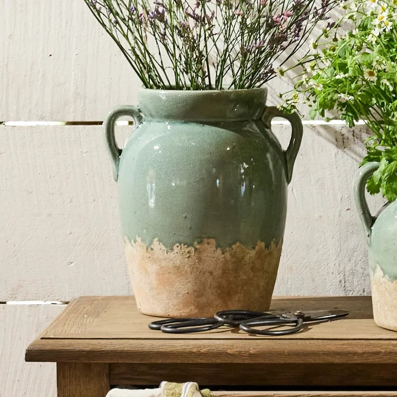 Tall pale blue and terracotta vase with handles displaying dried flowers