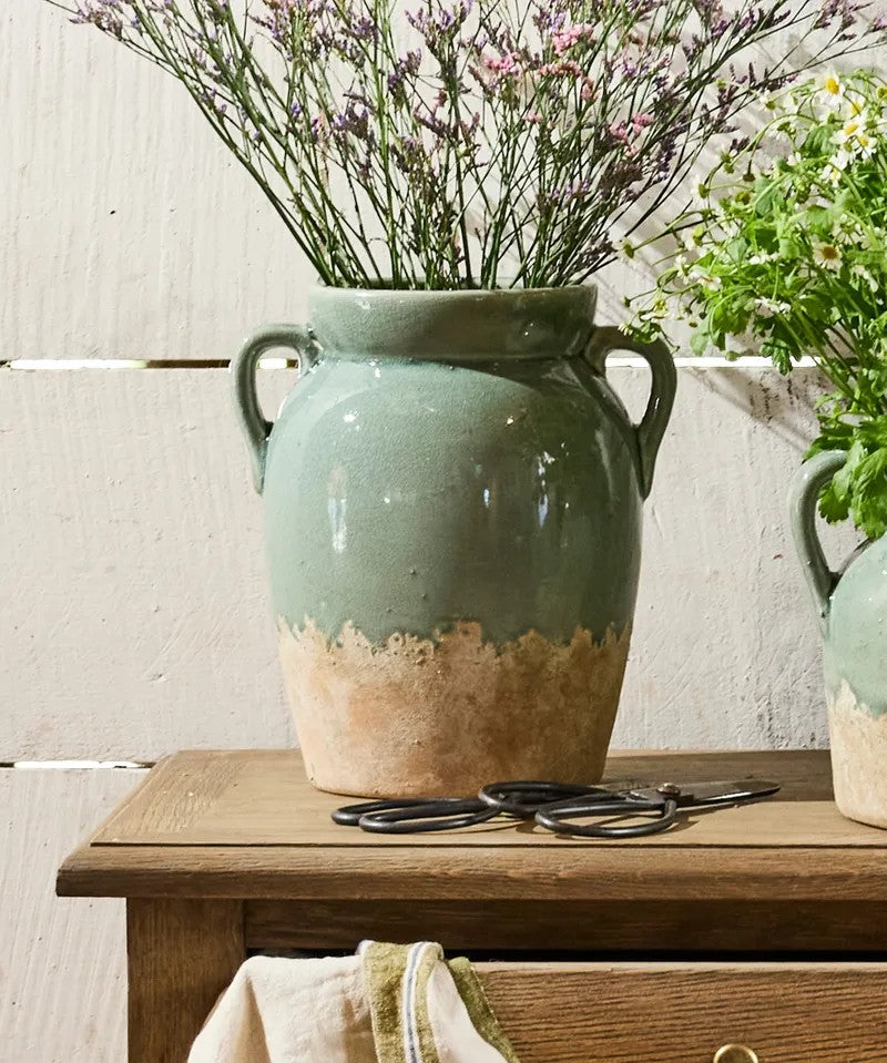 Tall pale blue and terracotta vase with handles displaying dried flowers