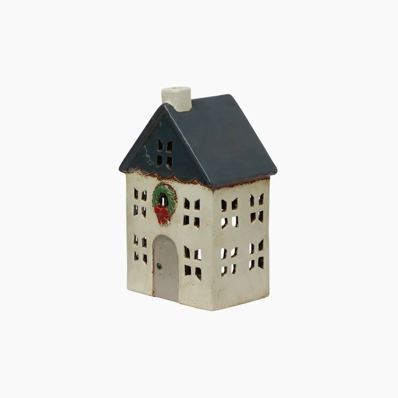 Small cream ceramic tealight house with a blue roof and green wreath on the front.