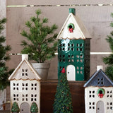 Decorative ceramic tealight houses with Christmas trees and red holly berries on a wooden surface.