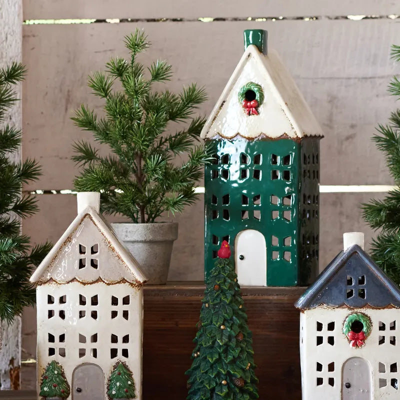 Decorative ceramic tealight houses with Christmas trees and red holly berries on a wooden surface.