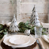 Table setting with decorative metal trees trees and greenery against a wooden wall.
