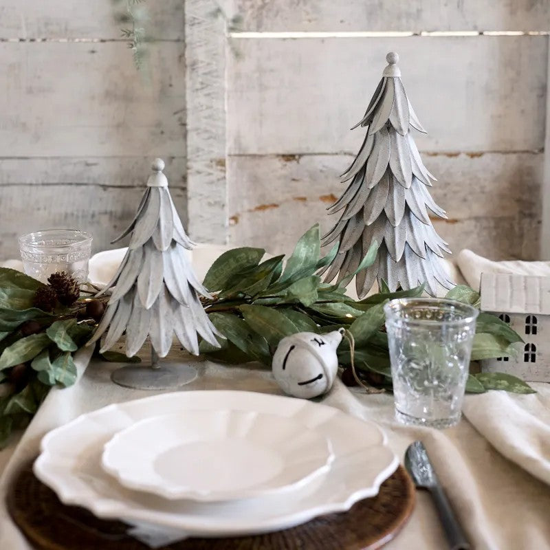Table setting with decorative metal trees trees and greenery against a wooden wall.